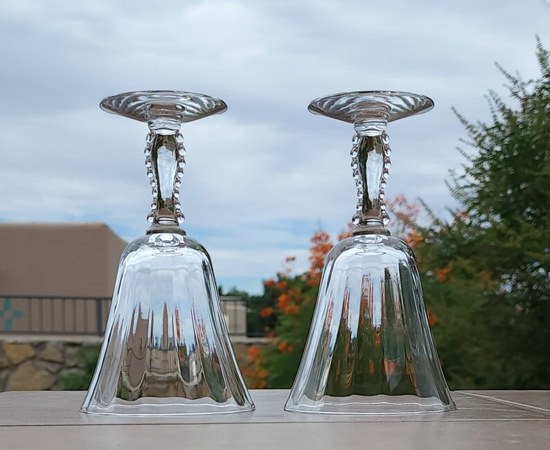 May include: Two clear glass bell-shaped drinking glasses with a beaded stem and a fluted design.