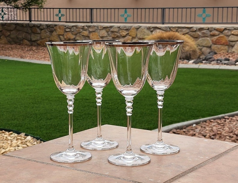 May include: Four clear glass wine glasses with a silver rim and a gold band around the top. The glasses have a beaded stem.