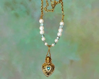 May include: A gold necklace with a heart-shaped pendant. The pendant is decorated with a green gemstone and intricate details. The necklace is made with white pearls and blue beads.