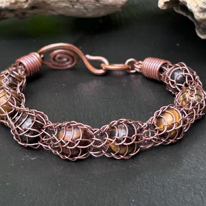 May include: A copper wire wrapped bracelet with tiger's eye beads. The bracelet has a spiral clasp.