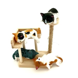 May include: A miniature wooden cat tree with a sisal-wrapped post and four small cat figurines. One black and white cat sits on top, while a calico, a dark gray tabby, and an orange and white cat are positioned on the lower wooden platforms.
