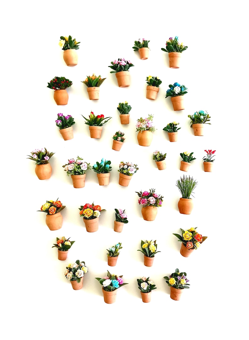 May include: A collection of miniature terracotta pots, each containing a variety of small artificial flowers and greenery in diverse colors including pink, yellow, blue, red, and white, arranged in a scattered pattern against a plain white background.