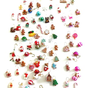 May include: A large collection of Christmas-themed stitch markers featuring miniature charms including gingerbread people, candy canes, Santa Claus figures, decorated houses, Christmas trees, stockings, and colorful ornaments with metal loops.