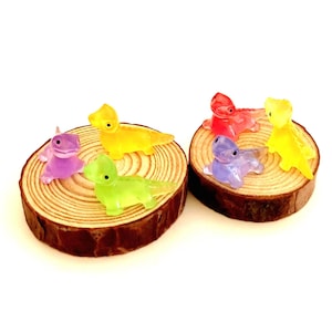 May include: Six miniature glass lizards in various colors, including purple, green, yellow, and red, are displayed on two small wooden rounds.