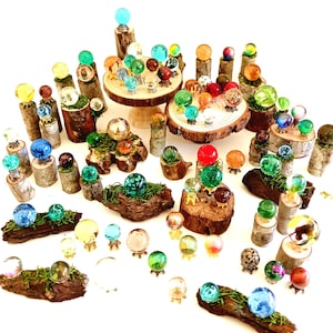 May include: A collection of colorful glass orbs on wooden bases. The orbs are displayed on various wooden platforms, including logs and tree stumps. Some of the orbs are on small gold stands.