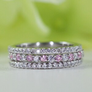 May include: A silver band ring with three rows of small, clear and pink gemstones.