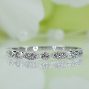 May include: A silver band ring with a row of small, oval-shaped diamonds set in a delicate design.