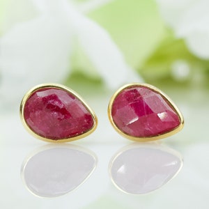 Könnte beinhalten: Ein Paar goldene Ohrringe mit roten rubinroten tropfenförmigen Steinen.