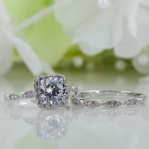 May include: A silver engagement ring set with a large, round, clear cubic zirconia stone surrounded by smaller stones. The band is also set with smaller stones.