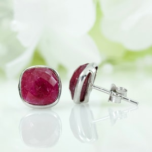 May include: A pair of silver stud earrings with a square-shaped red gemstone.