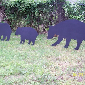 May include: Three black bear silhouettes made of metal, standing on a grassy lawn. The bears are different sizes, with the largest bear in the back and the smallest bear in the front.