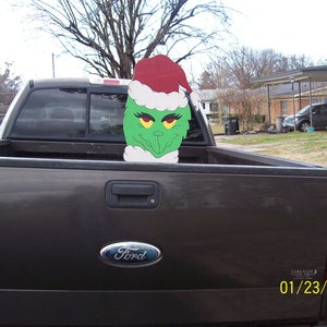 May include: A brown pickup truck with a Ford logo on the tailgate. A green Grinch character wearing a red Santa hat is in the truck bed.
