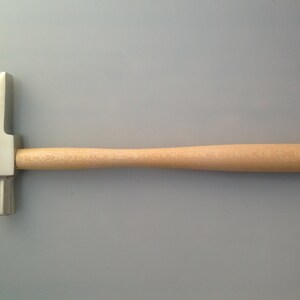 May include: A silver hammer with a wooden handle. The hammer has a rounded head and a smooth, polished finish.