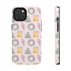 May include: A pink phone case with a repeating pattern of nutcrackers, Christmas trees, wreaths, and bells. The case is designed for a smartphone with a camera bump.