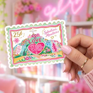 May include: A rectangular sticker shaped like a postage stamp featuring a colorful illustration of Salvation Mountain. The design includes the text 'GOD IS LOVE', '25¢', 'Salvation Mountain', and 'SAY JESUS I'M A SINNER PLEASE COME UPON MY BODY AND INTO MY HEART'.