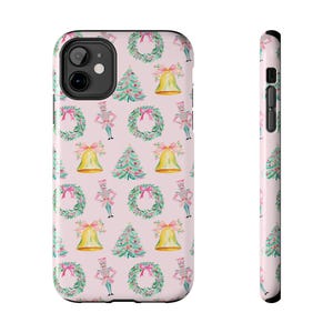 May include: A phone case with a light pink background featuring a repeating pattern of watercolor-style Christmas trees, green wreaths with pink bows, gold bells with pink bows, and nutcracker figures in pink and blue uniforms.