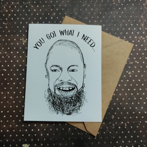 May include: A white greeting card with a black and white illustration of a smiling person with a beard. The card reads "YOU GOT WHAT I NEED..." and is placed on a brown envelope. The background is a brown surface with white polka dots.