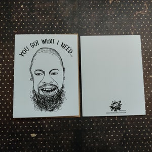 May include: Greeting card with a black and white illustration of a smiling face with a beard and the text "YOU GOT WHAT I NEED...". The card is blank on the inside and has a logo on the back.
