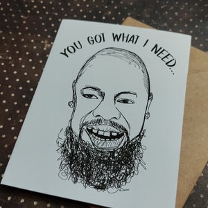 May include: A black and white greeting card with a hand-drawn illustration of a smiling face with a beard. The text "YOU GOT WHAT I NEED..." is above the face. The card is paired with a brown envelope.