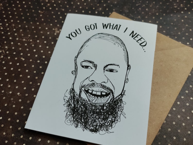 May include: A black and white greeting card with a hand-drawn illustration of a smiling face with a beard. The text "YOU GOT WHAT I NEED..." is above the face. The card is paired with a brown envelope.