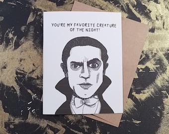 May include: A black and white greeting card featuring a stylized illustration of a vampire with the text "YOU'RE MY FAVORITE CREATURE OF THE NIGHT!". The card is paired with a brown envelope.