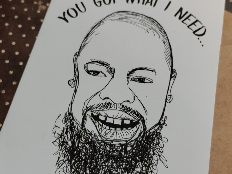 May include: A black and white line drawing of a smiling person with a beard. The text "YOU GOT WHAT I NEED..." is above the person's head. The drawing is on a white card.