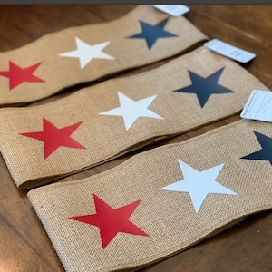 May include: Three burlap ribbon rolls with three stars each. The stars are red, white, and black.
