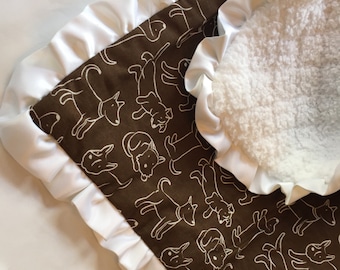 May include: A brown baby blanket with a white satin trim and a white sherpa lining. The blanket features a repeating pattern of white dogs.