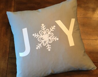 May include: A light blue throw pillow with the word "JOY" in white letters and a white snowflake design in the center.