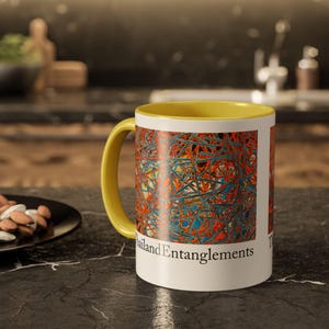 Puede incluir: Una taza de cerámica blanca con un borde amarillo y un diseño abstracto colorido. La taza tiene el texto "Thailand Entanglements" impreso en la parte inferior.