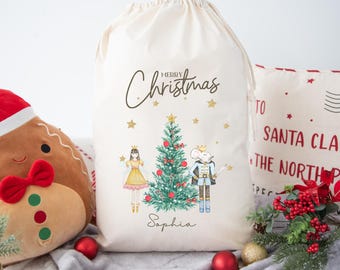 May include: A cream-colored Christmas gift bag with a drawstring closure. The bag features a watercolor illustration of a Christmas tree, a princess, and a nutcracker. The words "Merry Christmas" and a name are printed on the bag.