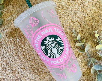 May include: A clear plastic reusable cup with a pink design featuring the text "I'm the nail tech they told you about" and a stylized green Starbucks logo. The cup has a green straw.