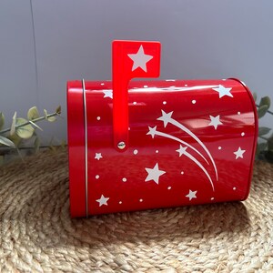 May include: Red metal mailbox with a white star design and a red flag with a white star. The mailbox is decorated with white stars and shooting stars.
