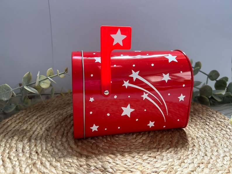 May include: Red metal mailbox with a white star design and a red flag with a white star. The mailbox is decorated with white stars and shooting stars.