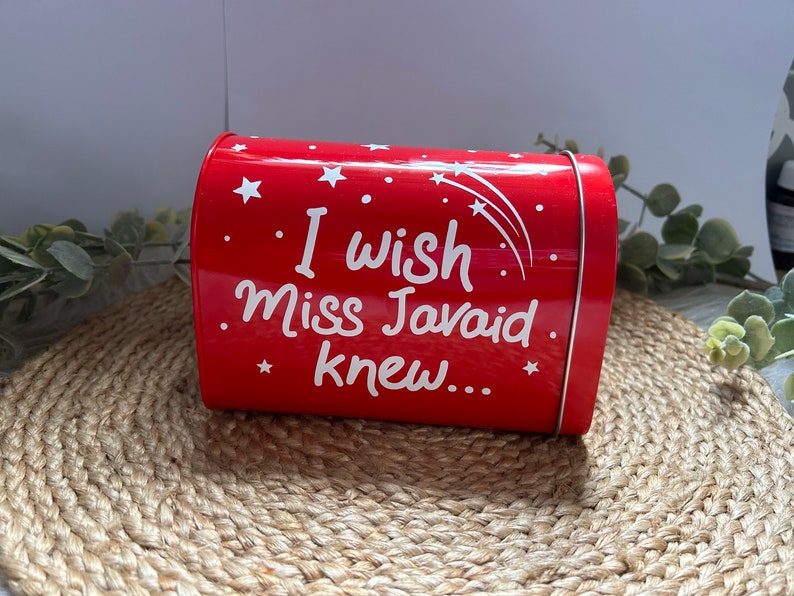 May include: Red metal tin with a white inscription that reads "I wish Miss Javaid knew..." with white stars and shooting stars on the tin.