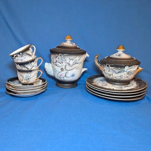 May include: A tea set featuring a tall lidded teapot, a lidded sugar bowl, and three teacups with matching saucers. Each piece is crafted from white ceramic with a black gradient finish, gold accents, and a detailed raised dragon motif.