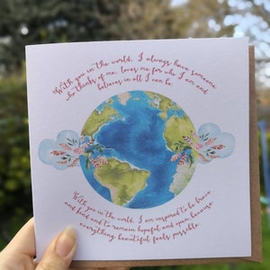 May include: A card with a watercolor illustration of the Earth with pink hearts and floral accents. The text reads "With you in the world. I always have someone who thinks of me, loves me for who I am and believes in all I can be. With you in the world. I am inspired to be brave and kind and to remain hopeful and open, because everything beautiful feels possible."