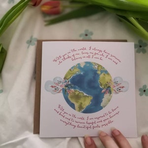 May include: A white card with a watercolor illustration of the Earth and pink flowers. The card has the text "With you in the world. I always have someone who thinks of me, loves me for who I am and believes in all I can be." and "With you in the world. I am inspired to be brave and kind and to remain hopeful and open. Everything beautiful feels possible."