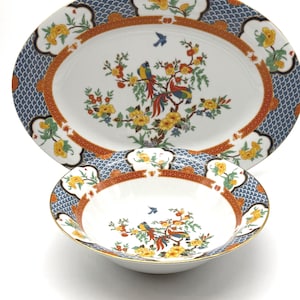 May include: An oval serving platter and a round bowl with a floral and bird design. The white porcelain pieces have a blue, orange, and yellow pattern around the edges. The center of each piece features a colorful bird and floral motif.