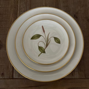 May include: Three white ceramic plates with a gold rim. The smallest plate has a green and pink floral design.
