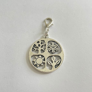 May include: Silver charm with a circular design featuring four seasons: a tree, a snowflake, a sun, and a plant.