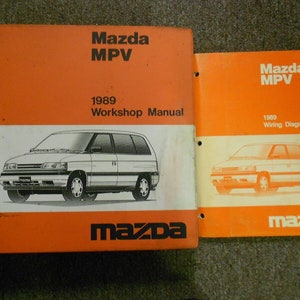 Puede incluir: Dos manuales Mazda MPV naranja y blanco. El manual más grande está etiquetado como "1989 Workshop Manual" y presenta una ilustración en blanco y negro de un Mazda MPV. El manual más pequeño está etiquetado como "1989 Wiring Diagram". El logotipo de Mazda es visible.