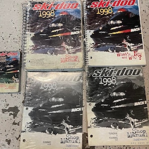 May include: Four black and white shop manuals for Ski-Doo snowmobiles from 1998. The manuals include a Shop Manual, Shop Manual Supplement, and a What's New and Why? booklet. The manuals feature images of Ski-Doo snowmobiles, including the Summit x670, Tundra R Touring SLE, and Mach 1.
