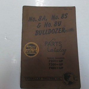 May include: A brown cover for a Caterpillar Tractor Company parts catalog for the No. 8A, No. 8S, and No. 8U bulldozers. The cover has a gold "Master Catalog" sticker and the text "Serial Numbers 72D1-UP, 73D1-UP, 74D1-UP".