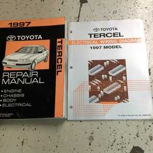 Könnte beinhalten: Zwei Reparaturhandbücher für einen Toyota Tercel aus dem Jahr 1997. Das Handbuch links ist ein allgemeines Reparaturhandbuch mit einem Bild eines silbernen Tercel auf dem Cover. Das Handbuch rechts ist ein Handbuch für elektrische Schaltpläne mit einem Schema einer Leiterplatte auf dem Cover.