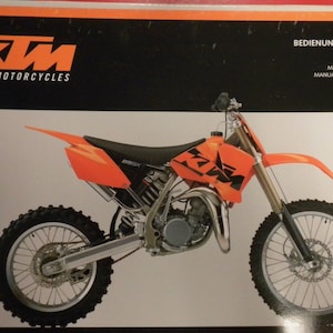 Puede incluir: Una moto de cross KTM 85 SX negra y naranja con un asiento negro y un motor plateado. La moto está sobre un fondo blanco. La imagen incluye el texto "SPORTMOTORCYCLES" y "BEDIENUNGSANLEITUNG" en texto negro sobre un fondo blanco. El texto "OWNER'S MANUAL", "MANUALE D'USO", "MANUEL D'UTILISATION" y "MANUAL DE INSTRUCCIONES" está en texto negro sobre un fondo blanco. El texto "2003" está en texto negro sobre un fondo blanco.