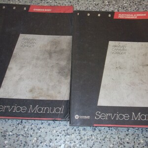 May include: Two 1985 Chrysler Ram Van, Caravan, and Voyager service manuals. The manual on the left is for the chassis and body. The manual on the right is for the electrical and engine performance.