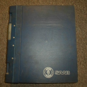 Puede incluir: Una carpeta azul con una columna vertebral de metal plateado y un logotipo Saab blanco con el texto "SAAB" impreso debajo.