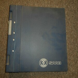 Puede incluir: Una carpeta azul con un mecanismo de anillas de metal plateado. La carpeta tiene un logotipo blanco con el texto "SAAB" y un logotipo más pequeño con el texto "SCANIA".