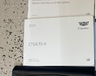 May include: Two white Cadillac owner's manuals, one for the 2019 Cadillac Limited Warranty and Owner Assistance Information and the other for the 2019 CTS/CTS-V. The manuals are closed and sitting on a gray concrete surface.